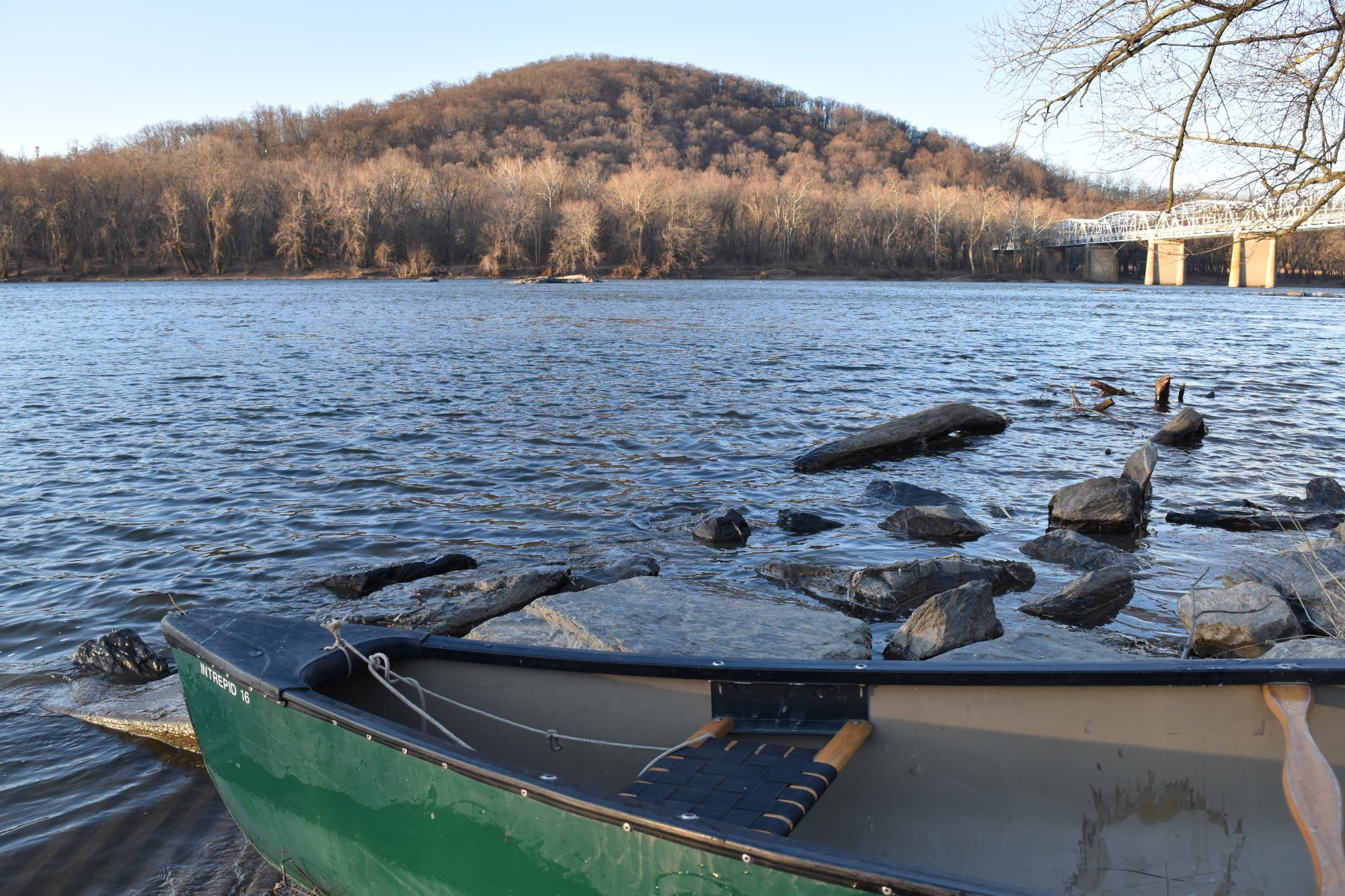 A canoe on the shoreline of the river with a winter forest in the background.