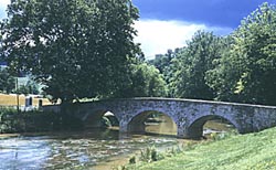 The image is of an old stone bridge that crosses a river. The bridge has three archways.