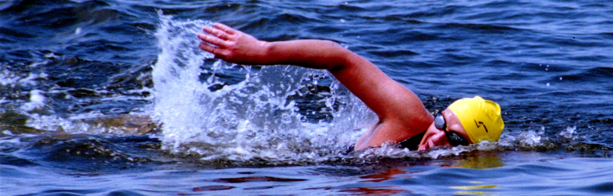 The profile of a person swimming with their right arm out of the water.