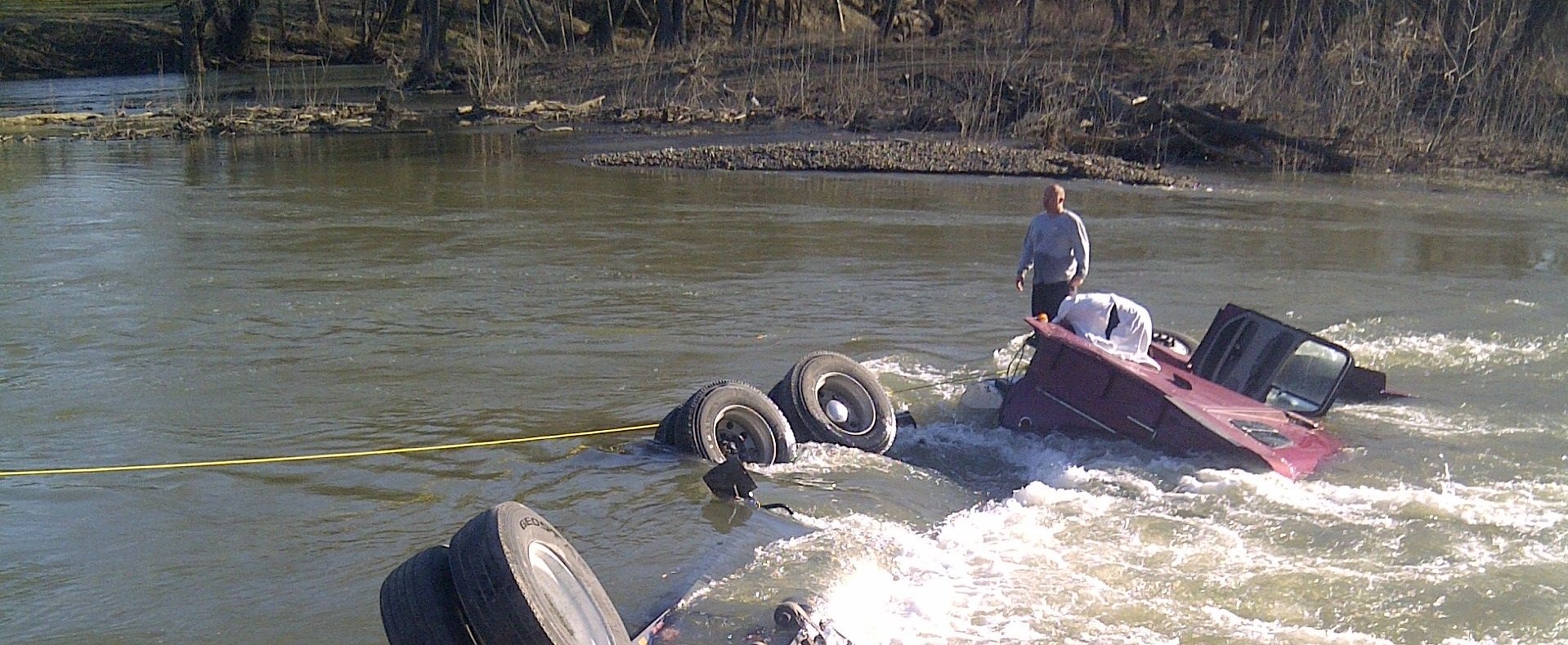 A truck laying on its side, mostly under water in a river.