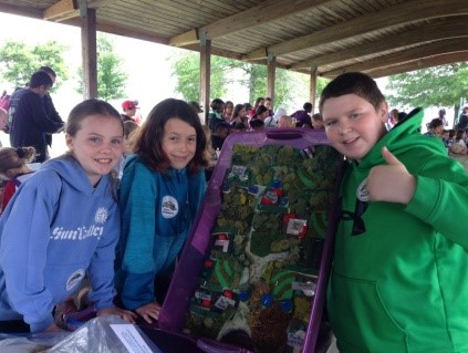 Three students holding up a watershed model in an outdoor pavilion. One student in a green sweatshirt is giving the "thumbs up" sign.