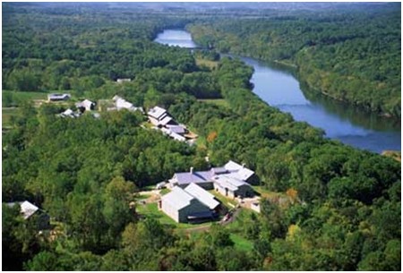 An aerial view of a river surrounded by forestland. There are some houses and buildings in the foreground.