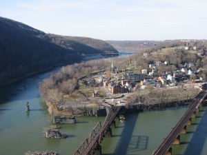 An aerial view of two rivers meeting. Two train track bridges are seen leading into a small town.
