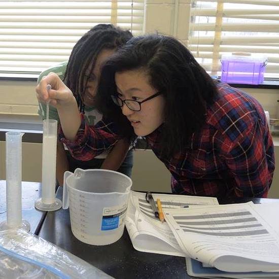 Two female high school students using a pipette to transfer water.
