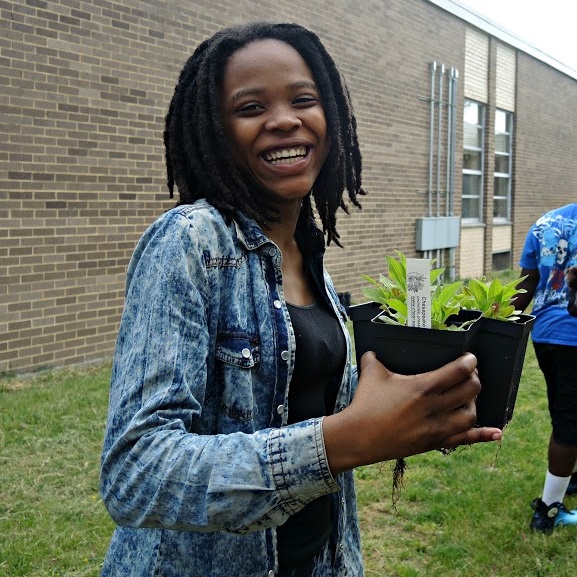 A smiling student holding two plants.