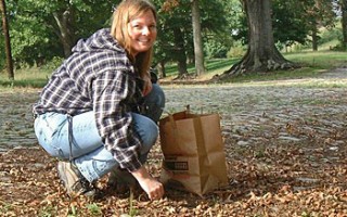 A woman crouching, putting acorns into a paper bag.