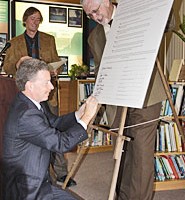 A man kneeling down to sign a large sheet of paper.