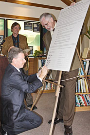 A man kneeling down to sign a large sheet of paper.
