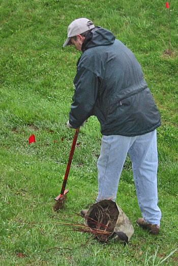 A man leaning on a tool to plant a tree.