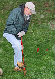 A man leaning a tool to plant a tree.