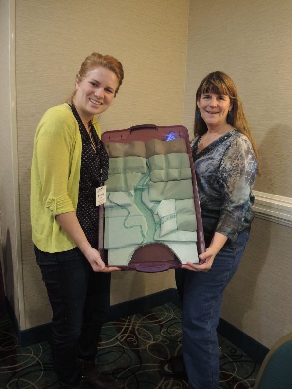Two women holding up a half-finished watershed model with just styrofoam.
