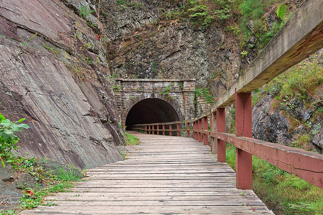 A wooden walking path that leads into a tunnel in the side of a mountain.