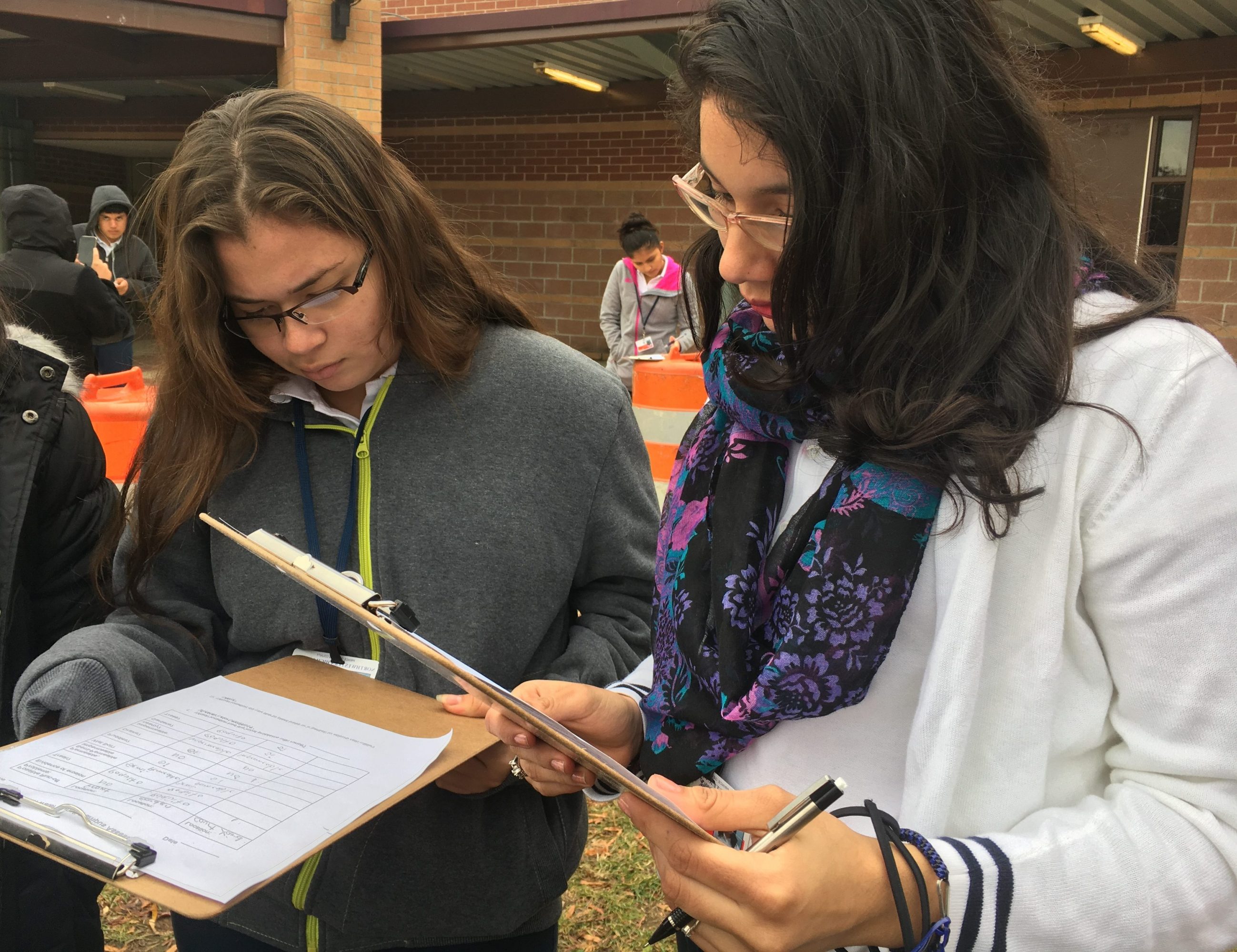 Two female high school students looking at clipboards.