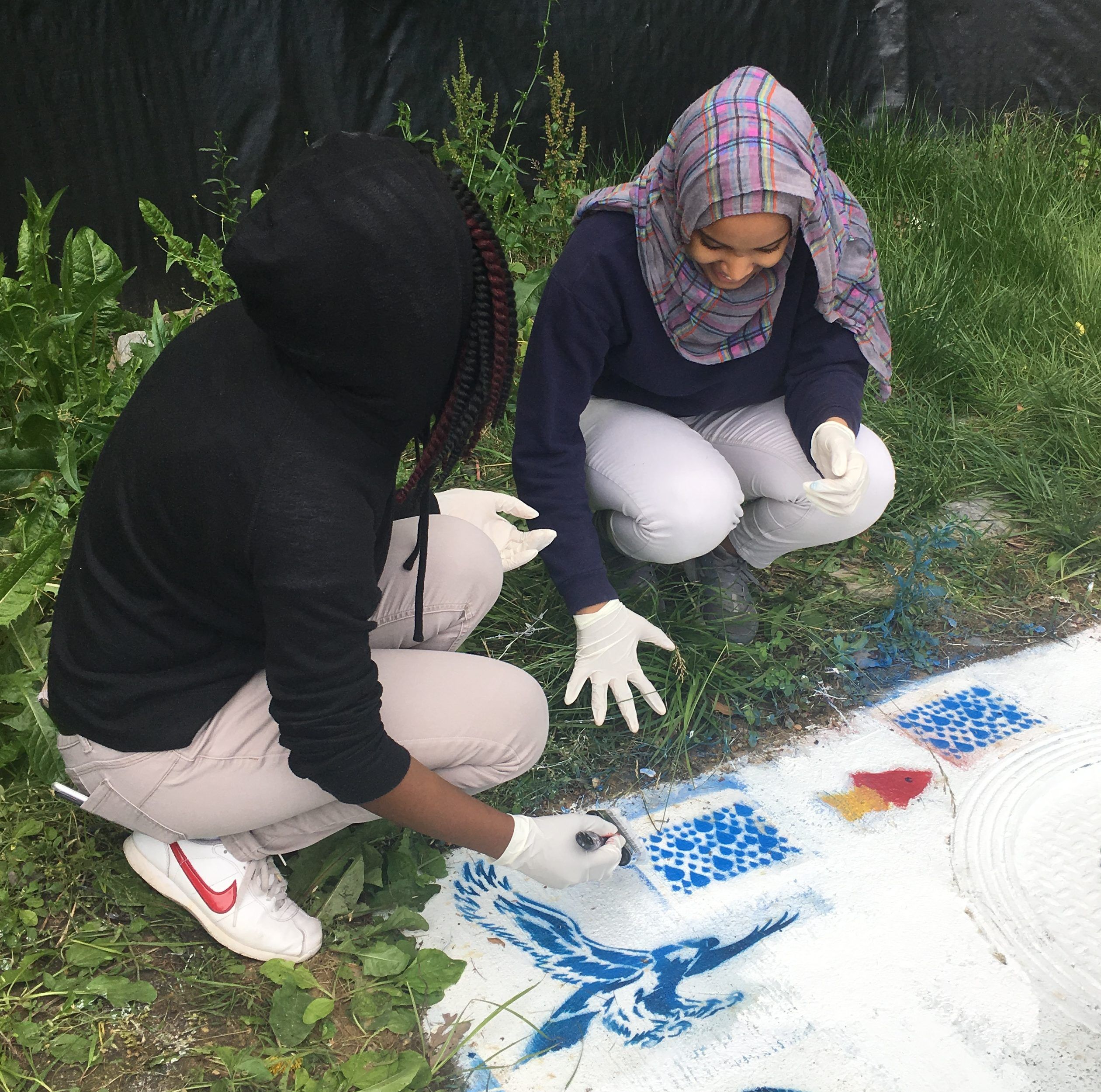 Two female students kneeling to paint a stormwater drain.