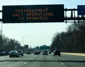 Cars driving on a freeway below a sign that reads: Pretreatment Salt Operations in Progress