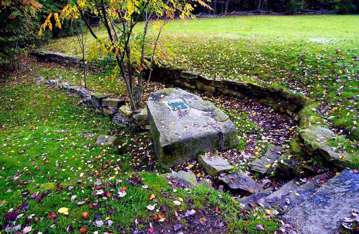 A large stone surrounded by smaller stones. The large stone has a plaque on it that tells the story of Fairfax Stone.
