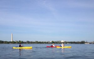 Three kayakers in the Potomac river in front of D.C. monuments