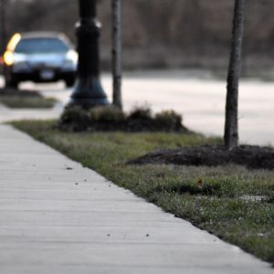 A close-up of a sidewalk, with the road and a car in the foreground.