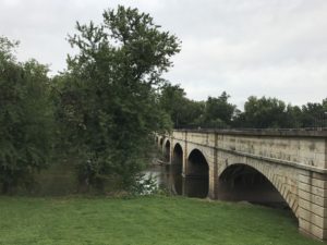 The Monocacy Aqueduct on the right. Trees on the left. Green grass in the foreground. 