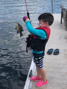 A little boy is holding up a fishing pole with a fish on the hook.