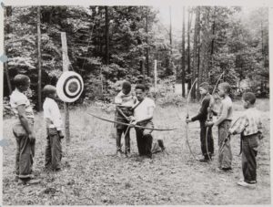 Young black boys receiving an archery lesson.