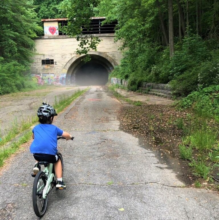 Boy riding into an abandoned tunnel. Lush vegetation on both sides of the trail.