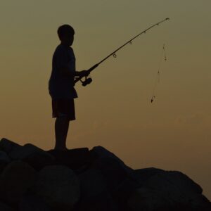 Silhouette of a young boy fishing at sunset. 