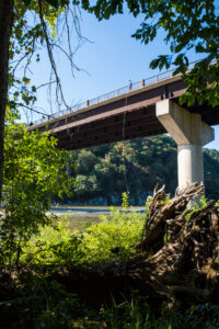 Scientist sends testing equipment attached to a rope over the side of a bridge. Shenandoah river is below the bridge.