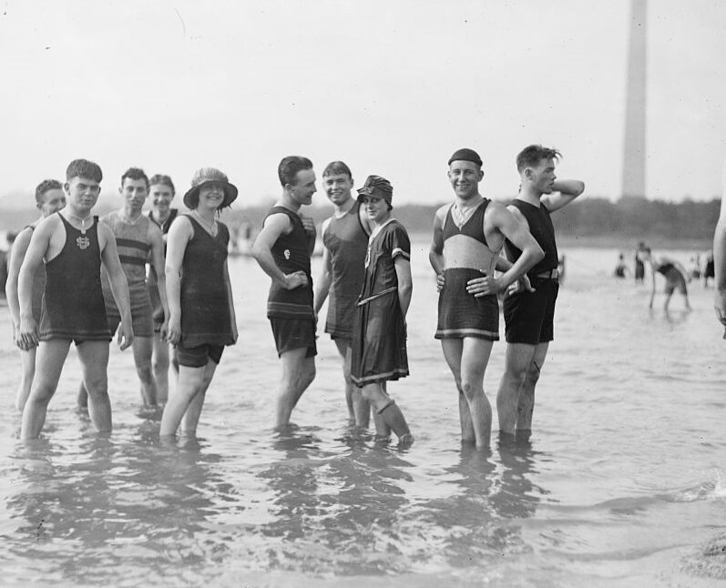 People in old fashioned swimsuits stand in the water of the tidal basin / Potomac River.