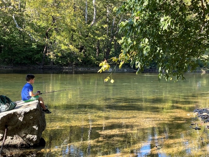 Young boy with a fishing pole sitting on a rock in the Shenandoah River.