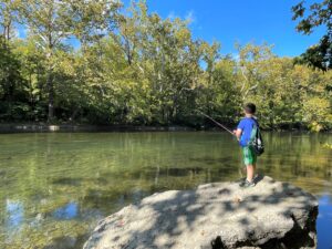 Young boy stands with a fishing pole on a rock next to the Shenandoah River. 