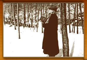 A vintage photo of a man with a dark jacket standing in the snow, holding a camera. 