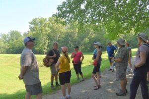 Man stands next to a path in a wooded area with other hikers standing near him.