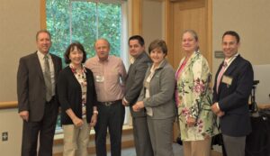 Seven people stand in front of a conference room, smiling. 